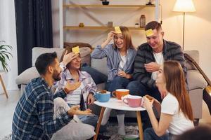 jugando quién soy yo juego. grupo de amigos tienen una fiesta en el interior juntos foto