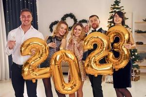 2023 balloons in hands. Group of people have a new year party indoors together photo