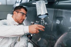 Process of painting the car. Man in uniform is working in the auto service photo