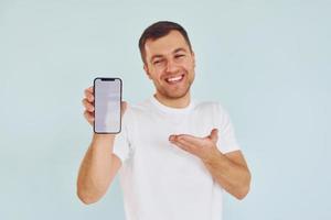 hombre con ropa informal parado en el estudio con el teléfono en las manos foto