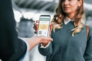 Vaccination certificate in the phone. Young female tourist is in the airport at daytime photo