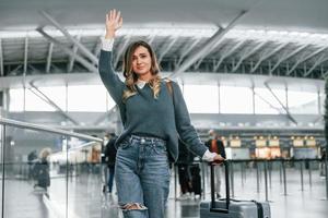 Hello gesture. Young female tourist is in the airport at daytime photo