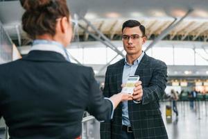 sosteniendo y mostrando el certificado de vacunación. un joven hombre de negocios con ropa formal está en el aeropuerto durante el día foto