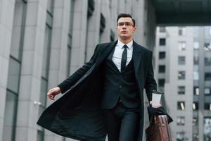 Walking forward. Businessman in black suit and tie is outdoors in the city photo