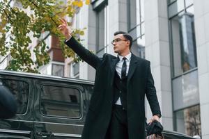 Calling taxi. Businessman in black suit and tie is outdoors in the city photo