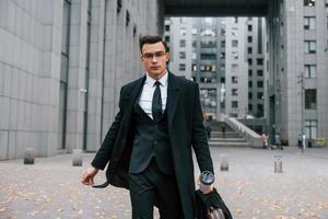 Walking forward. Businessman in black suit and tie is outdoors in the city photo