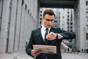 Checking the time. Businessman in black suit and tie is outdoors in the city photo