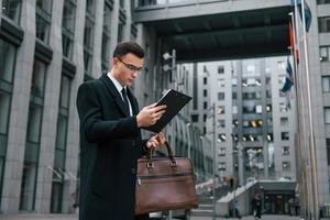 Conception of formal clothes. Businessman in black suit and tie is outdoors in the city photo