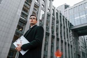 Grey building behind. Businessman in black suit and tie is outdoors in the city photo