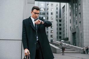 Standing near the building. Businessman in black suit and tie is outdoors in the city photo