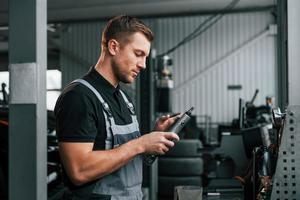 Holding tool. Man in uniform is working in the auto service photo