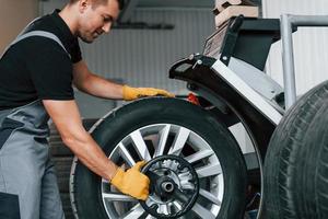 Fixing the tire. Man in uniform is working in the auto service photo