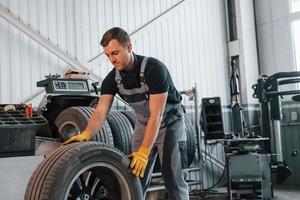 Walking with tyre. Man in uniform is working in the auto service photo