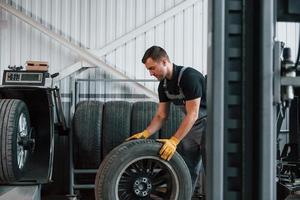 Working with broken wheel. Man in uniform is working in the auto service photo
