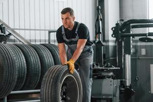 Walking with tyre. Man in uniform is working in the auto service photo