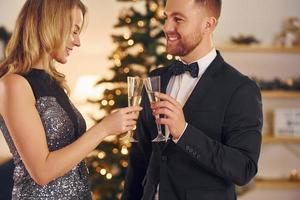 Cheering with glasses of alcohol. Happy couple have a new year party indoors together photo