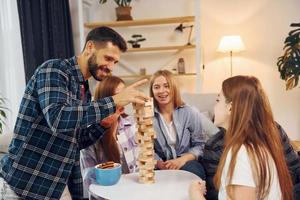 Wooden tower game on the table. Group of friends have party indoors together photo