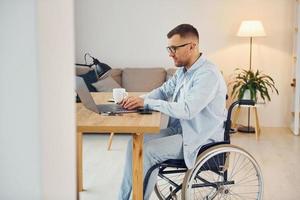 Working by using laptop. Disabled man in wheelchair is at home photo