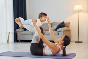 Woman laying down on mat and holding little girl. Mother with her little daughter is at home together photo