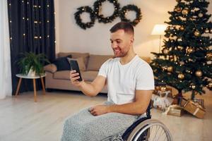 Using smartphone to communicate with people. New year is coming. Disabled man in wheelchair is at home photo