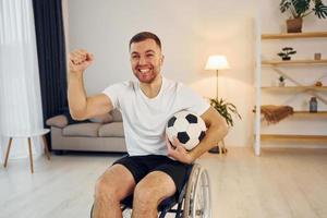 Soccer fan with ball. Disabled man in wheelchair is at home photo