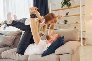 Laying down on the sofa. Father with his little daughter is at home together photo