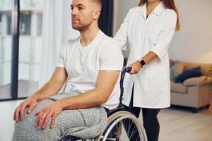 trabajador medico la mujer está ayudando. hombre discapacitado en silla de ruedas está en casa foto