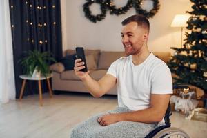 Using smartphone to communicate with people. New year is coming. Disabled man in wheelchair is at home photo