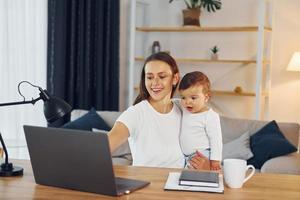 Sitting by the table with laptop. Mother with her little daughter is at home together photo