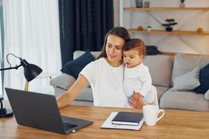 Sitting by the table with laptop. Mother with her little daughter is at home together photo