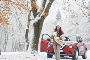 emociones alegres. bella joven está al aire libre cerca de su automóvil rojo en invierno foto