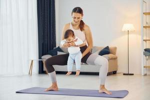 parado en la colchoneta y haciendo ejercicios. madre con su pequeña hija está en casa juntos foto