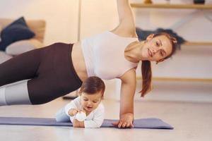 Woman doing exercises. Mother with her little daughter is at home together photo