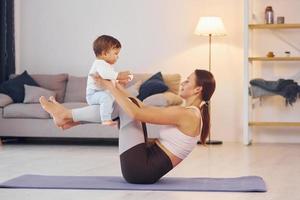 Focused at yoga exercises. Mother with her little daughter is at home together photo