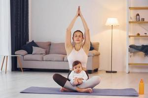 en la estera de yoga. madre con su pequeña hija está en casa juntos foto