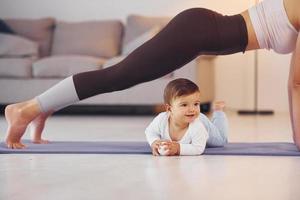 Woman doing exercises. Mother with her little daughter is at home together photo