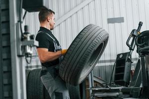 Walking and holding tyre. Man in uniform is working in the auto service photo