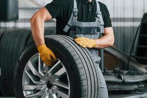 Walking and holding tyre. Man in uniform is working in the auto service photo