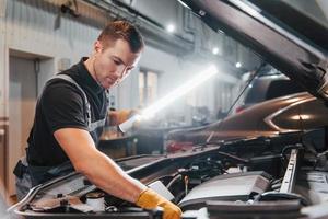 Under the hood. Man in uniform is working in the auto service photo