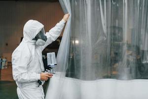 In protective white uniform. Man is working in the auto service photo
