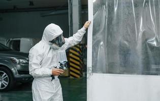 In protective white uniform. Man is working in the auto service photo