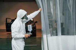 In protective white uniform. Man is working in the auto service photo