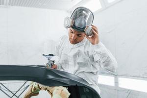 pintando el coche. el hombre de uniforme está trabajando en el servicio de automóviles foto