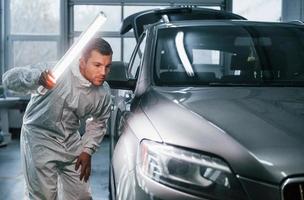 Silver colored car. Man in uniform is working in the auto service photo