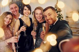 sosteniendo el teléfono. grupo de personas tienen una fiesta de año nuevo en el interior juntos foto