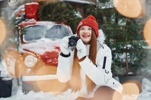 With camera in hands. Happy young woman standing outdoors and celebrating christmas holidays photo