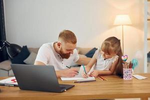 Using laptop. Father with his little daughter is at home together photo