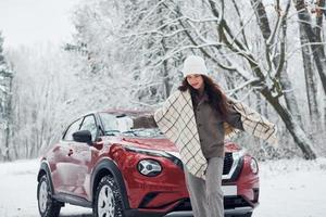 hermoso fondo de invierno. bella joven está al aire libre cerca de su automóvil rojo en invierno foto