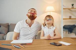 Sitting by the table and having fun. Father with his little daughter is at home together photo