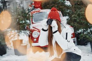 con cámara en manos. mujer joven feliz de pie al aire libre y celebrando las fiestas navideñas foto